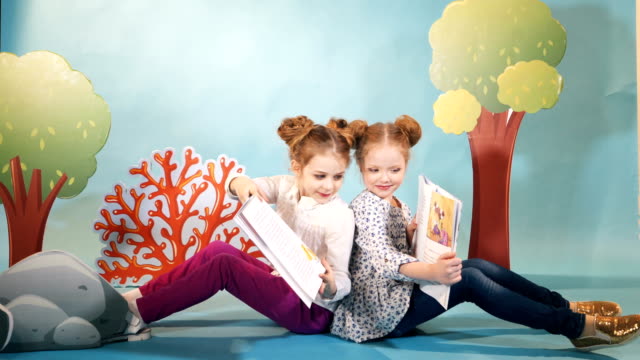 Two-little-girls-reading-a-book-on-a-blue-background.