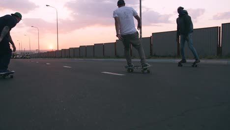 Grupo-de-jóvenes-skateboarding-en-la-carretera-en-el-temprano-por-la-mañana,-toma-cinematográfica,-cámara-lenta