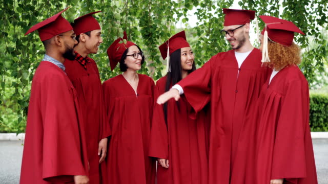 Feliz-graduación-grupo-multiétnico-de-los-estudiantes-es-unir-palmas-y-palmas-de-las-manos-celebrando-graduación-exitosa,-gente-llevan-vestidos-y-juntas-de-mortero.