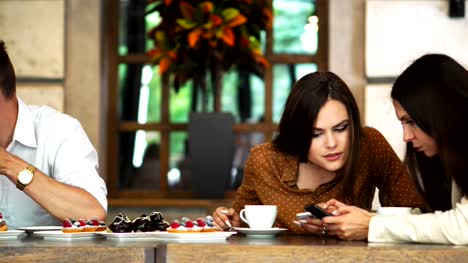 Multi-ethnic-group-of-young-friends-talking-and-using-smartphones-apps-on-wifi-in-cafe,-happy-millennial-people-having-fun-with-phones-sharing-coffee-house-table-enjoying-meeting-in-public-place