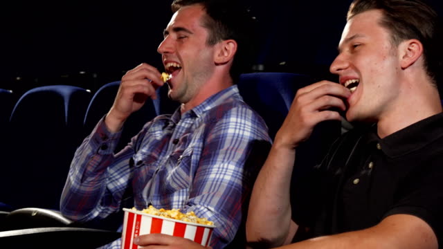 Male-friends-eating-popcorn-and-laughing-while-watching-comedies-at-the-cinema