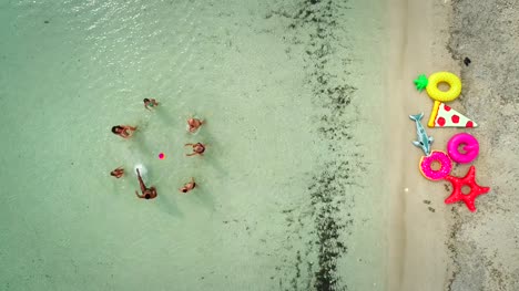 Aerial-view-of-group-of-friends-playing-volleyball-in-sea-by-sandy-beach.