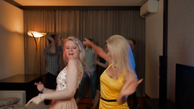Zwei-attraktive-sexy-Mädchen-tanzen-auf-Party-mit-ihren-Freunden-hinter