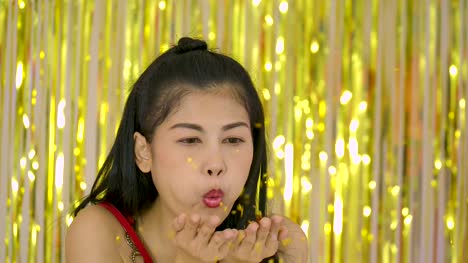 Beautiful-asian-woman-blowing-glitter-confetti-or-pieces-of-silver-foil-in-front-of-shiny-shimmer-curtain-background,-slow-motion.