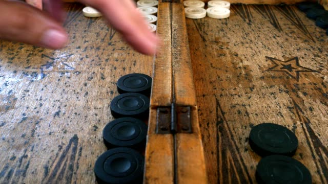 Zwei-junge-Männer-spielen-Backgammon-auf-einem-Holztisch-rollende-Würfel-und-verschieben-das-Stück.