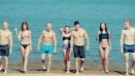 Group-of-friends-coming-out-of-the-water-on-the-beach.-Front-view
