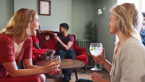 Dos-jóvenes-mujeres-blancas-adultas-sientan-riendo-juntos,-hablando-y-bebiendo-vino-en-el-salón-en-un-pub,-cerca