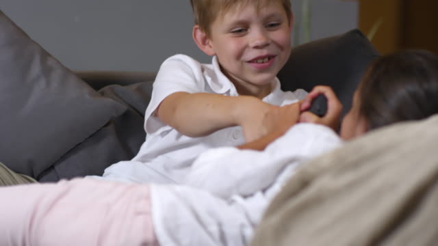 Kleine-Mädchen-und-Jungen-kämpfen-für-TV-Fernbedienung-auf-Sofa