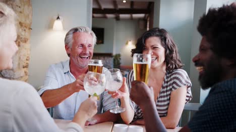 Senior-white-man-and-Hispanic-woman-sitting-at-a-table-in-a-pub-making-a-toast-with-colleagues,-close-up,-over-shoulder-view
