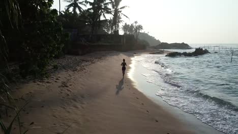 Two-healthy-lifestyle-young-women-friends-running-on-tropical-beach-during-sunrise-in-the-morning,aerial-drone-view-footage