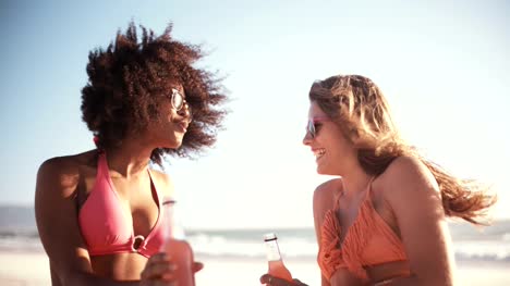 Girl-friends-en-bikinis-hablando-en-una-playa-con-alcopops
