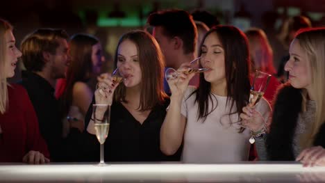Vier-attraktive-Mädchen-im-Verein-an-der-Bar-erhöhen-Ihre-Glas-Champagner-Gläser