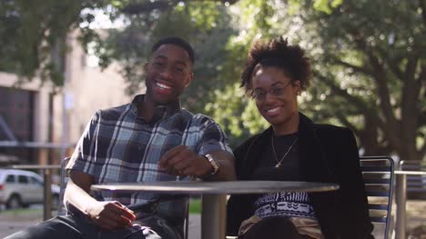 Afrikanische-amerikanische-Paar-an-einen-Tisch-im-freien-in-der-Stadt-reden-und-lachen-gemeinsam-mit-bokeh