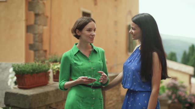 Dos-mujeres-jóvenes-atractivas-en-vestidos-de-verano-ligero-tienen-conversación-en-las-calles-de-la-ciudad-europea.