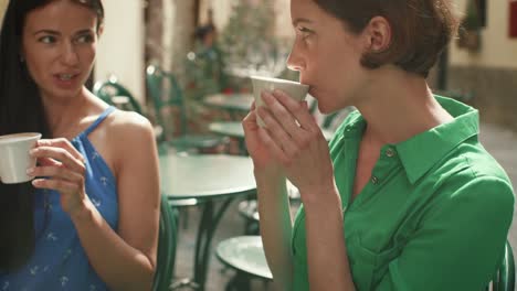 Dos-mujeres-jóvenes-atractivas-en-luz-verano-vestidos-relajante,-hablando-y-tomando-café-en-la-cafetería-de-la-calle.