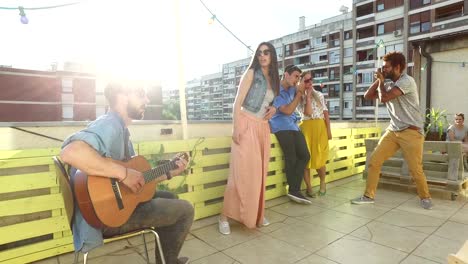 Amigos-divirtiéndose-en-la-terraza-de-la-azotea,-tocando-la-guitarra-y-tomando-fotos