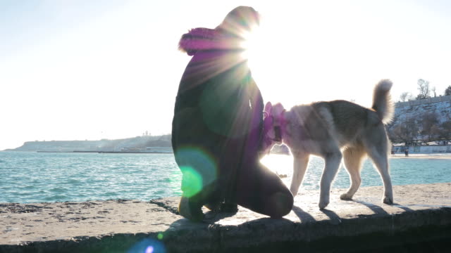 Young-woman-having-fun-with-siberian-husky-dog-on-sea-pier