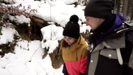 Young-man-and-woman-in-winter-clothing-walk-together-holding-hands-in-winter-forest.
