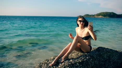 Young-happy-woman-chatting-with-friends-through-internet-using-smartphone-in-ocean-beach