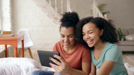 Two-mixed-race-young-funny-girls-talking-on-skype-on-tablet-computer-with-their-parents-at-home