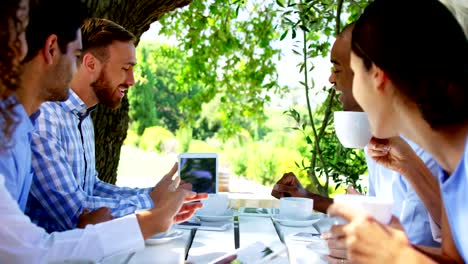 Group-of-friends-discussing-over-digital-tablet-at-outdoor-café