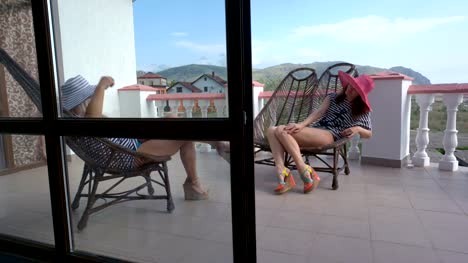 Two-women-relaxing-in-cane-chairs-on-open-terrace-balcony-at-vacation-home
