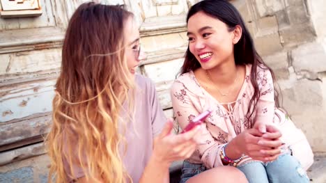 Mujeres-jóvenes-riendo-y-comprobación-de-los-medios-sociales-en-smartphone