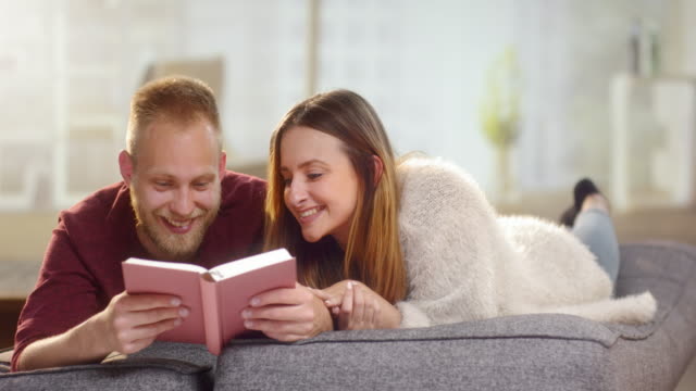 Young-sweet-couple-lying-on-a-couch-and-reading-a-a-funny-book