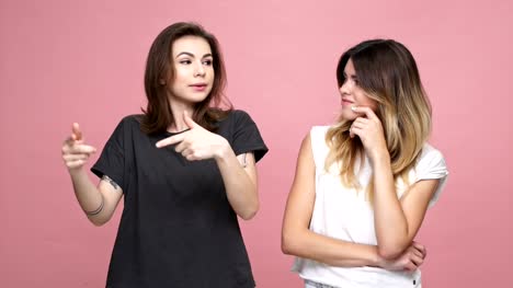 Young-pretty-girl-suggesting-ideas-to-her-doubting-unsure-female-friend-isolated-over-pink-background