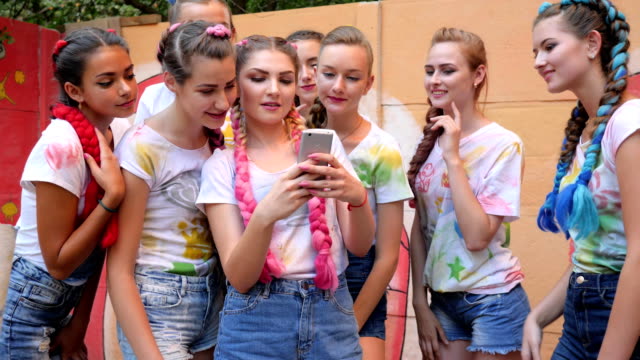crowd-of-girls-with-bright-braids-with-gadget-in-arms-on-open-air,-Laughing-team-of-youth-Looks-at-photos-on-phone