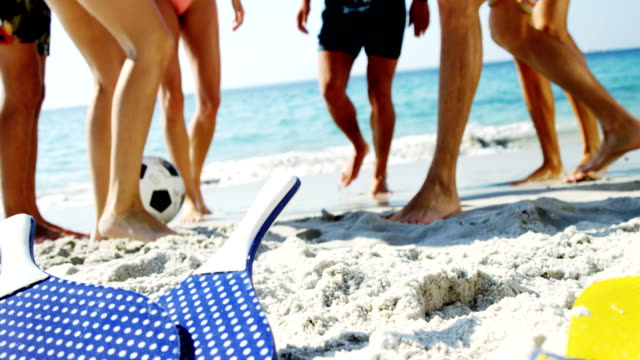 Low-section-of-friends-playing-football-at-beach