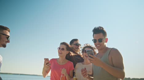 Jóvenes-divirtiéndose-en-la-playa-utilizando-teléfonos
