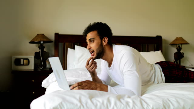 Mann-mit-Laptop-Computer-auf-Bett-Hispanic-liegend-Grübeln-Kerl-Typ-im-Chat-Online,-Schlafzimmer-morgens