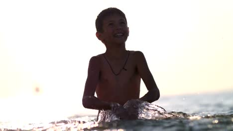 Jungen-spielen-mit-Wasser-im-Meer-bei-Sonnenuntergang,-spritzt