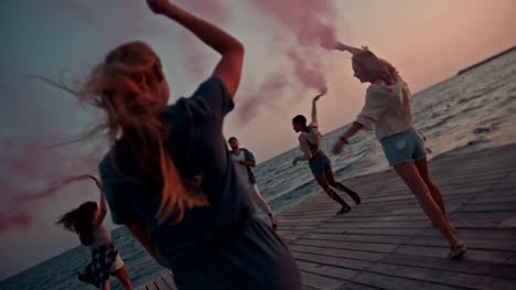 Multi-ethnic-friends-celebrating-with-smoke-bombs-on-jetty-at-sunset