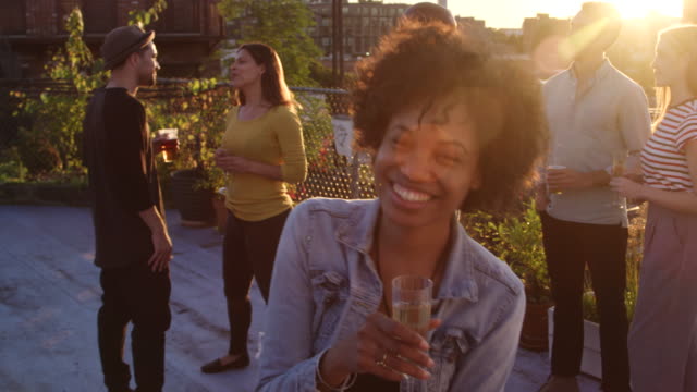 Young-black-woman-raising-a-glass-to-camera-at-rooftop-party