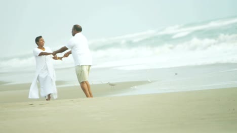 Retired-senior-ethnic-couple-dancing-together-on-beach