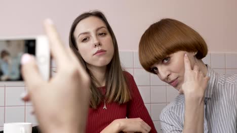 Young-beautiful-caucasian-girl-is-making-a-photo-on-the-smartphone-of-her-two-girlfriends-sitting-in-a-cafe.-Girls-are-posing.-Girlfriends-in-the-cafe-concept.-Using-a-smartphone-Close-up-60-fps