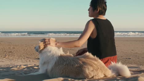 woman-petting-her-dog-on-the-beach-at-sunset