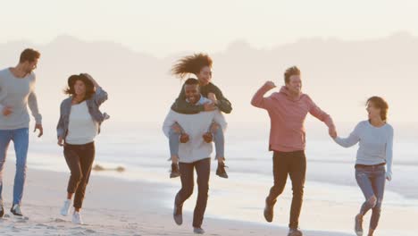 Gruppe-von-Freunden,-die-Spaß-am-Winter-Strand-zusammen-laufen