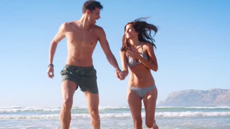 Slow-Motion-Schuss-des-Paares-im-Wellen-laufen-auf-Strandurlaub