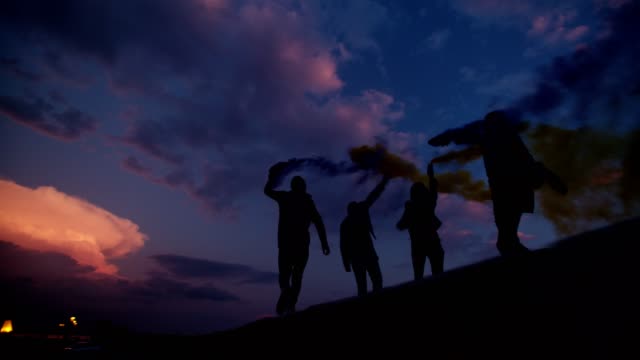 Group-of-young-friends-celebrating-with-smoke-bombs-after-sunset