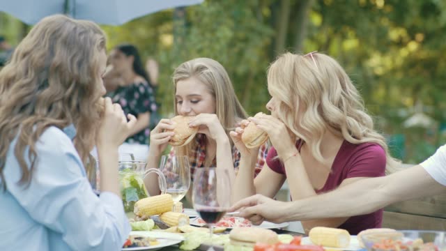 Freunde-Essen-Burger-sitzen-am-Esstisch-auf-Outdoor-Party