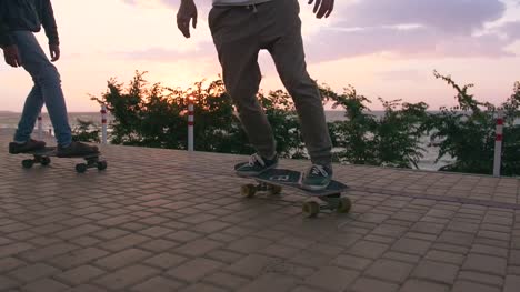 Group-of-young-people-skateboarding-on-the-road-in-the-early-morning-near-the-sea,-close-up-shot