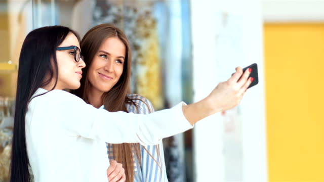 Zwei-Freundinnen-der-Schönheit,-die-dabei-einige-Einkaufsmöglichkeiten-in-modernen-Einkaufszentrum-und-nehmen-ein-Selbstporträt-mit-einem-smartphone