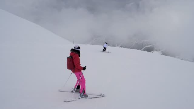 Two-Sporty-Female-Skiers-Skiing-On-The-Mountain-Downhill-In-Winter-In-Heavy-Fog