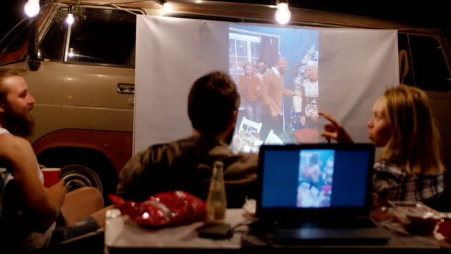 Amigos-ver-video-con-proyector-en-el-camping