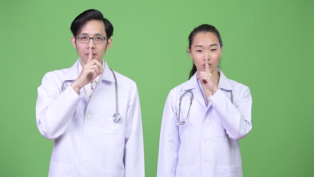 Médicos-de-la-joven-pareja-asiática-con-el-dedo-en-los-labios-juntos