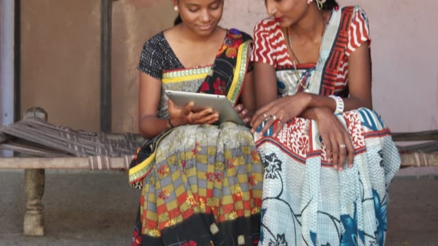 Hasta-dos-señoras-trabajando-y-discutiendo-importante-trabajan-de-preparación-en-una-tablet-con-pantalla-táctil-en-la-comodidad-de-su-casa-en-una-pequeña-ciudad-en-Rajasthan,-India-vestida-con-vestido-y-maquillaje-ropa-locales