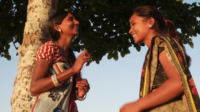 Handheld-stabilisierten-Schuss-zwei-Frauen-Mädchen-Geheimnisse-zu-teilen-und-ein-Scherz,-ein-Scherz-Spaß-Klatsch-Freiheit-unabhängige-Outdoor-Baum-Park-öffentliche-allein-Geheimnisse-versteckten-casual-Freunde-Buddy-Sari-Indien-Rajasthan